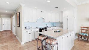 Una cocina con armarios blancos, una isla central con taburetes y una silla de madera.