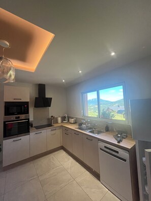A modern kitchen with built-in appliances, a large window with a view, and a ceiling light fixture. - Coc'oon, between the lake and the mountains, Serre Ponçon (Chorges)