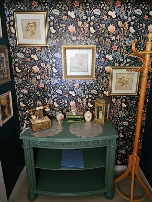 A room with floral wallpaper, a green console table with decorative items, and a wooden stand with a lantern. - Hidden Oasis - Pool & Gameroom Close to Downtown, Theme Parks & Springs (Orlando)