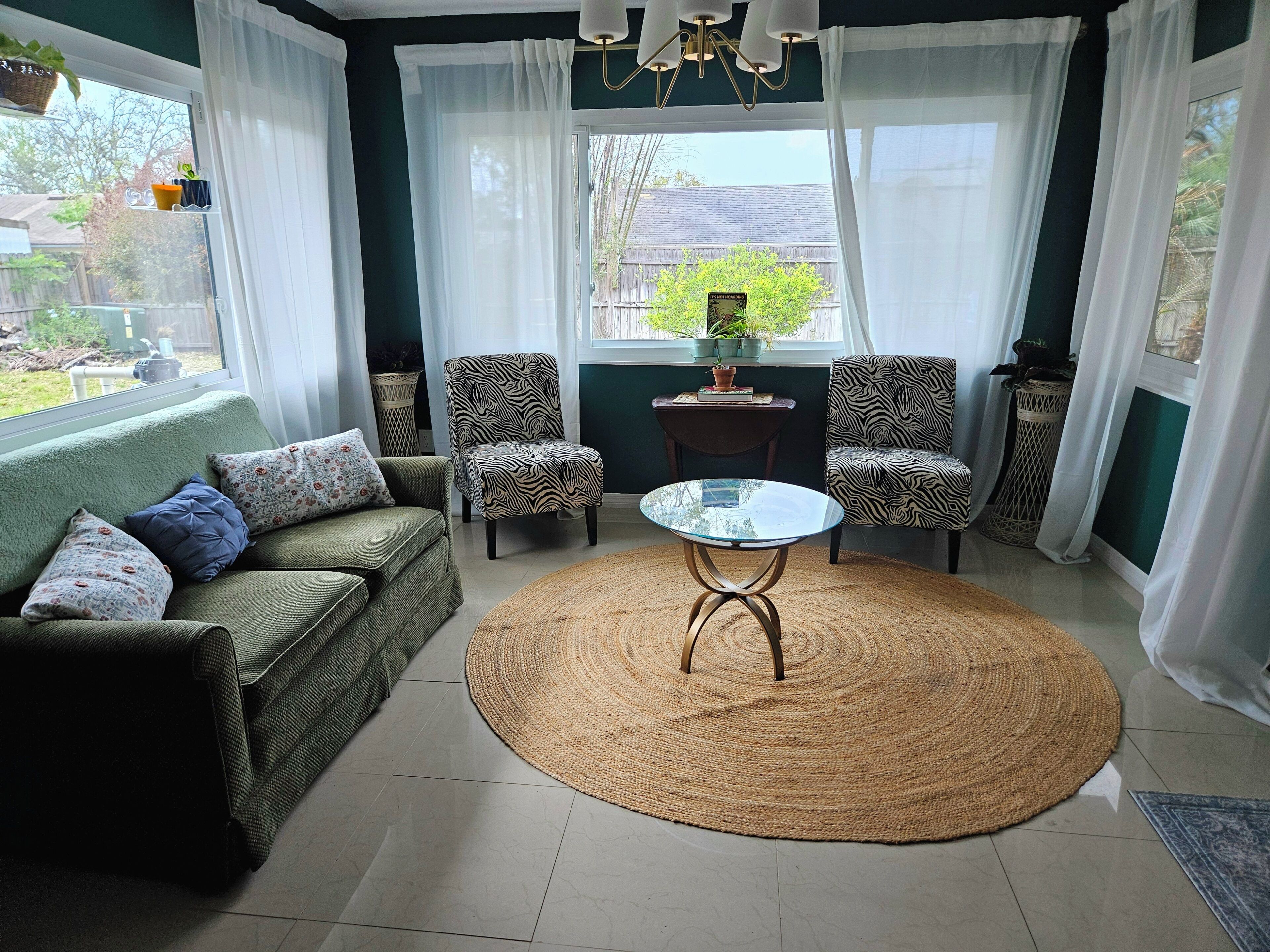A living room with a green sofa, two patterned armchairs, a glass coffee table, and a woven rug.