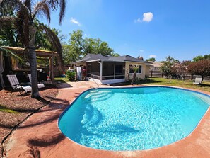 Ein Swimmingpool mit überdachter Terrasse, ein Haus und ein eingezäunter Garten.
