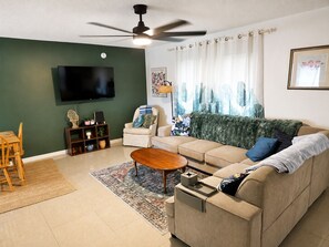 A living room with a sofa, coffee table, TV, and a ceiling fan. - Hidden Oasis - Pool & Gameroom Close to Downtown, Theme Parks & Springs (Orlando)