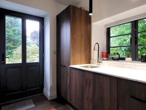 A modern kitchen with a dark wood cabinet, a white countertop, a built-in sink, and a window with a view of greenery. - Sweden Bothy, Ambleside (Ambleside)