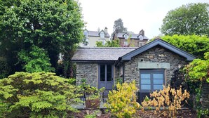 Una casa de piedra con techo oscuro, rodeada de abundante vegetación y un jardín cuidado.