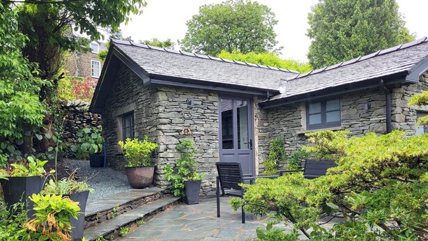 Una casa de piedra con un sendero de piedras que lleva a una puerta, rodeada de follaje y plantas en macetas.