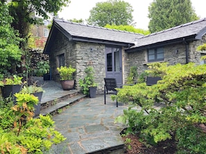 A stone house with a stone pathway leading to a door, surrounded by greenery and potted plants. - Sweden Bothy, Ambleside (Ambleside)