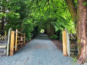 A gravel pathway flanked by stone walls and wooden gates, leading through a lush green forest. - Sweden Bothy, Ambleside (Ambleside)
