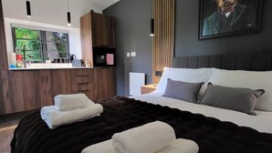 Un dormitorio moderno con una cama grande, un aparador de madera, un cuadro y vistas al verdor por la ventana.