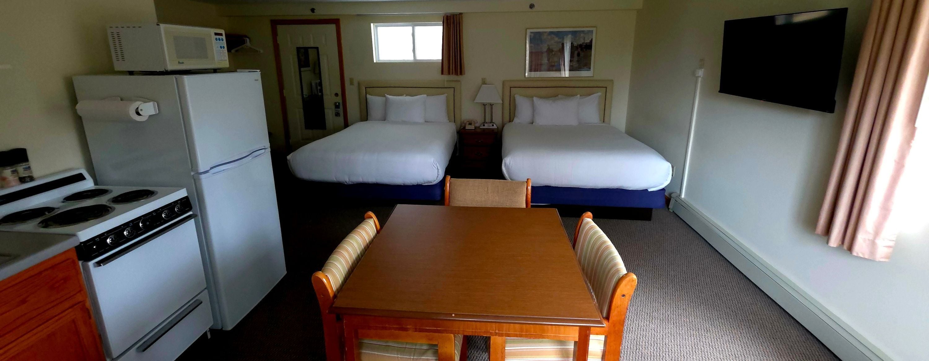 Een hotelkamer met een kitchenette, twee bedden, een televisie en een raam.