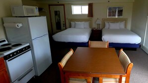 A hotel room with a kitchenette, two beds, a TV, and a window. - Wilson Lake Inn & Suites (Wilton)