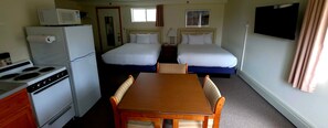 A hotel room with a kitchenette, two beds, a TV, and a window. - Wilson Lake Inn & Suites (Wilton)