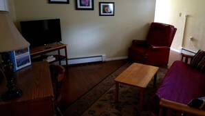 Uma sala de estar com televisão, uma cadeira vermelha, uma mesa de madeira e um sofá roxo.