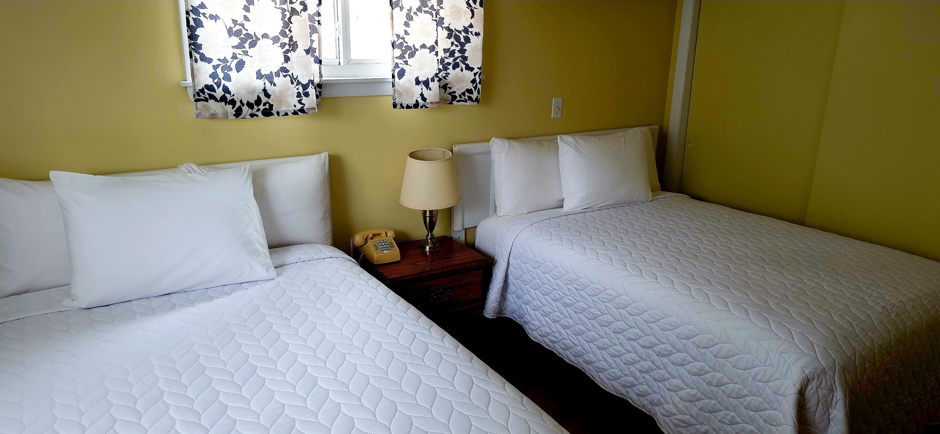 Una cama doble con ropa de cama blanca, una mesita de noche con lámpara y un teléfono.