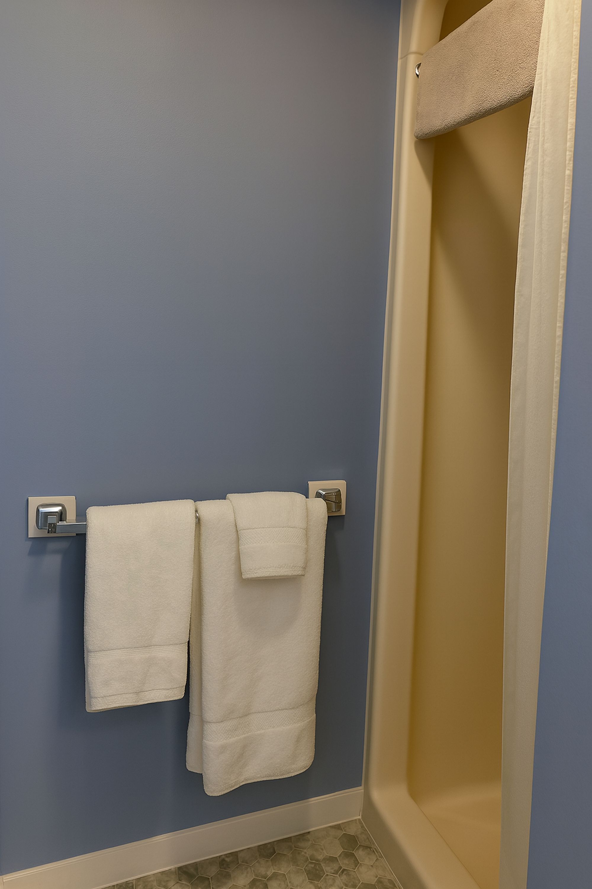 Ett badrum med en blå vägg, ett beige badkar och två vita handdukar som hänger på ett metallhandduksställ.