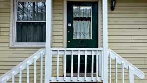 A house with a green door, white porch railing, and a window with a white curtain. - Wilson Lake Inn & Suites (Wilton)