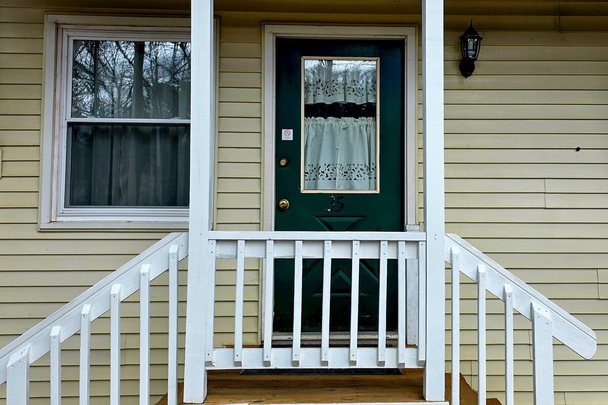 A house with a green door, white porch railing, and a window with a white curtain.
