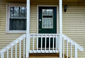 A house with a green door, white porch railing, and a window with a white curtain. - Wilson Lake Inn & Suites (Wilton)