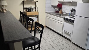 Uma cozinha com armários brancos, fogão, geladeira, mesa de jantar com cadeiras e cafeteira.