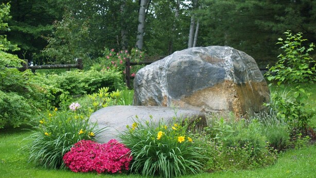 A large rock surrounded by lush greenery and flowering plants. - Wilson Lake Inn & Suites (Wilton)