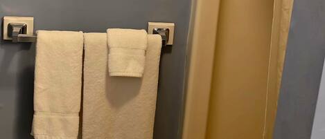 A bathroom with a towel rack holding two towels, a shower with a beige curtain, and a hexagonal tile floor.