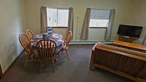 Uma sala de jantar com mesa, cadeiras, televisão e uma janela com cortinas.