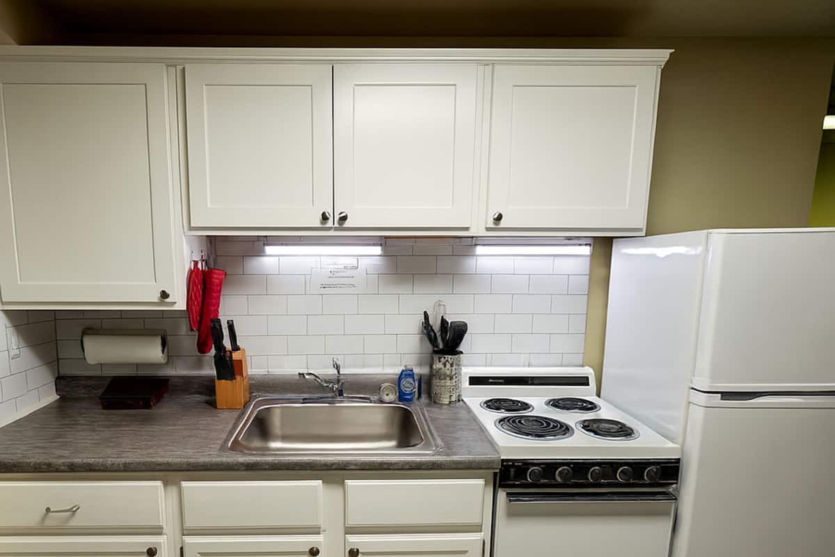 A kitchen with white cabinets, a stainless steel sink, a stove, and a refrigerator.