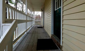 A covered wooden porch with a white railing, a door with the number 34, and a black doormat. - Wilson Lake Inn & Suites (Wilton)
