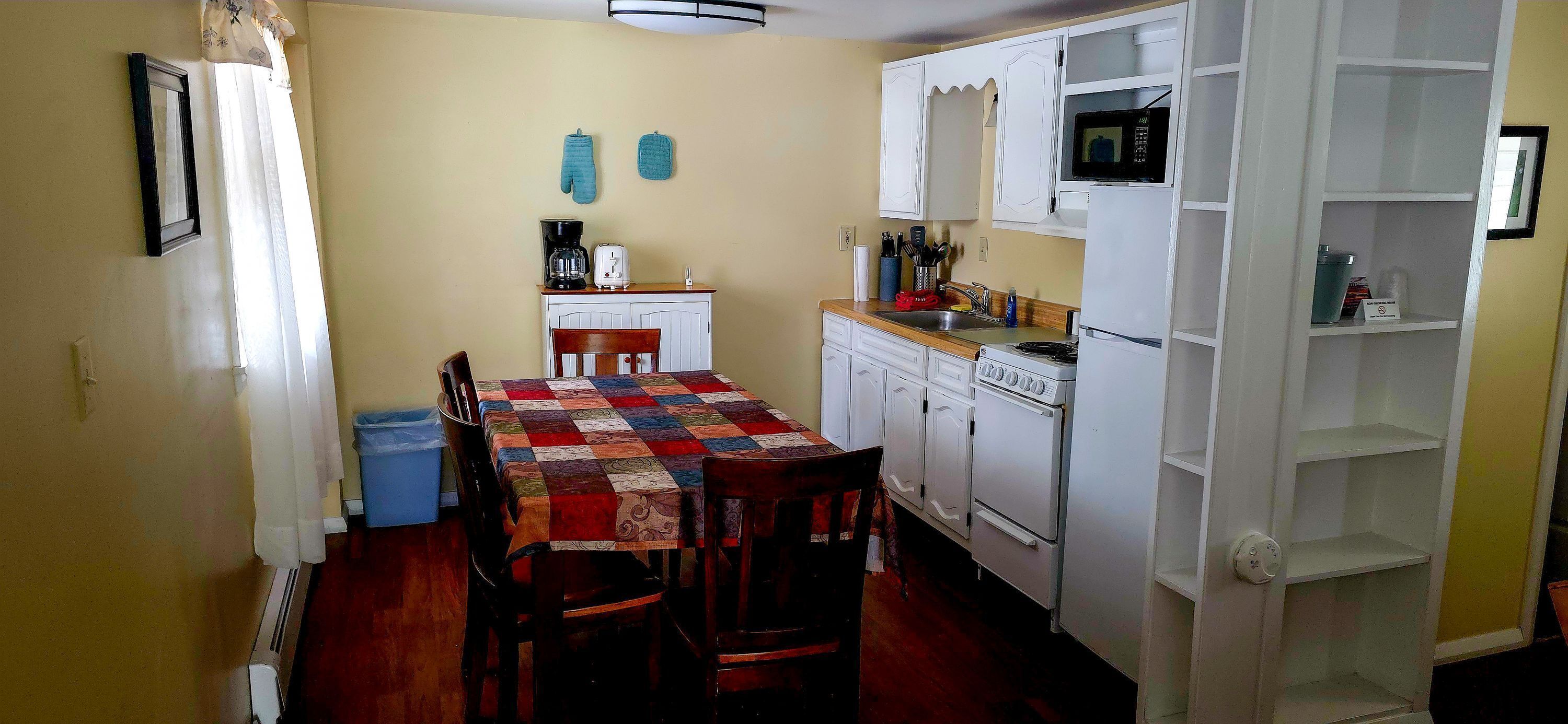 Una cucina compatta con mobili bianchi, un forno a microonde, una macchina per il caffè e un tavolo con sedie.