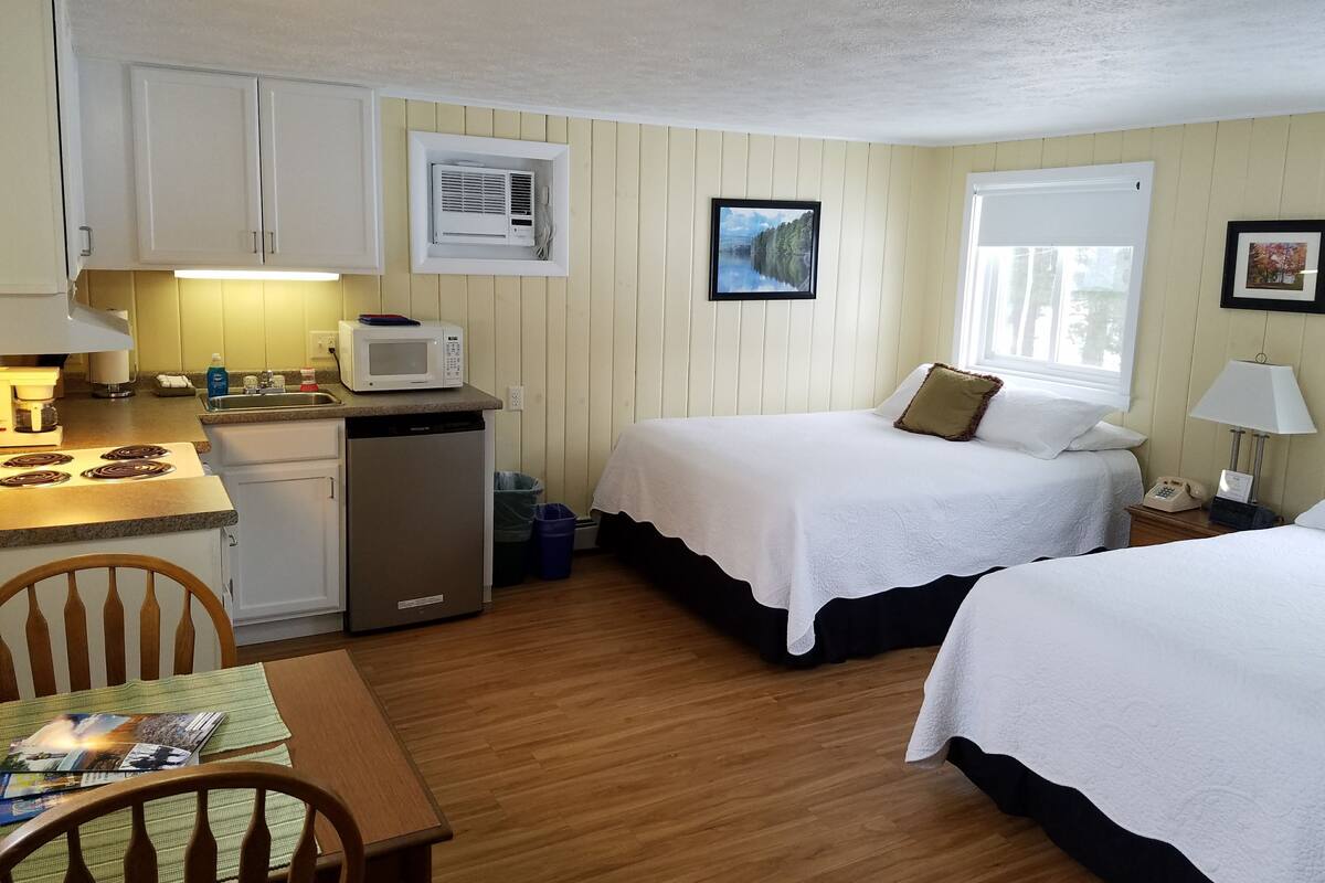 A compact room with a kitchenette, two beds, a dining table, and a chair.