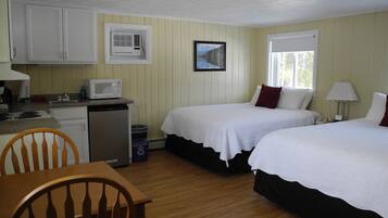 A room with two beds, a kitchenette, a dining table, and a window.