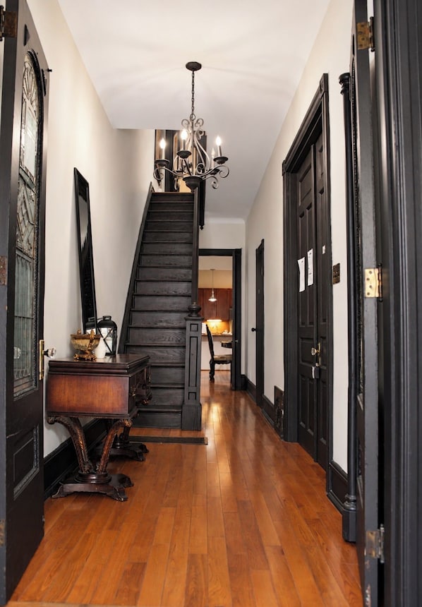 A wooden staircase with a chandelier, flanked by dark wooden doors and a polished wooden floor.