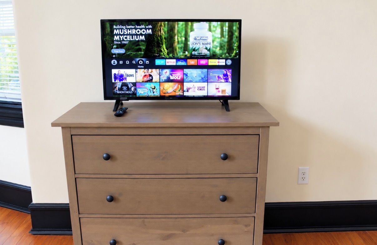 A television on a wooden dresser with a forest background on the screen.