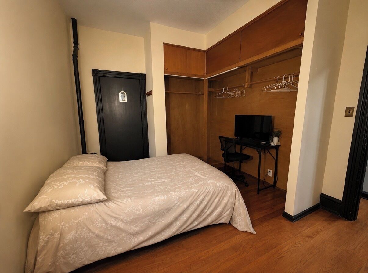 Un dormitorio con cama, armario con ropa colgada, escritorio con silla y televisión.
