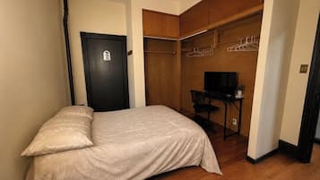 Un dormitorio con cama, armario con ropa colgada, escritorio con silla y televisión.