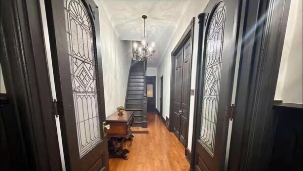 Un couloir doté d’un plancher en bois, d’un escalier et d’un lustre.