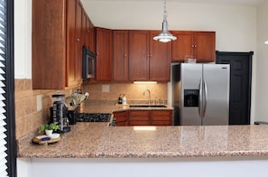 A kitchen with wooden cabinets, a stainless steel refrigerator, granite countertops, and a built-in stove.