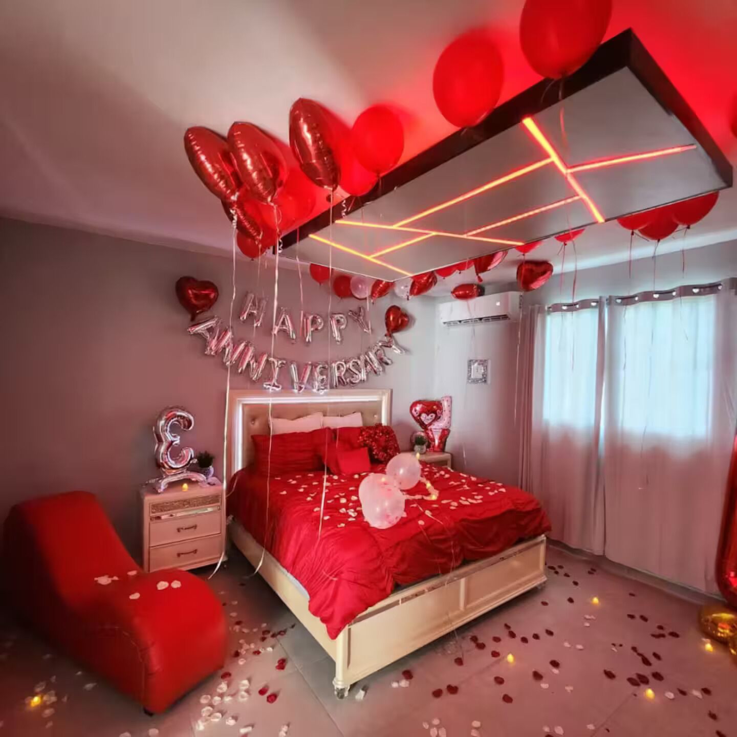 Une chambre à coucher avec un lit, une table de chevet, un fauteuil rouge et un mur orné d’une inscription « Joyeux anniversaire ».
