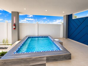 A rectangular swimming pool with blue-tiled edges, surrounded by a white fence and a blue wall with geometric patterns.