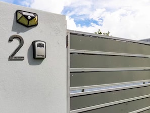 Een gevel met een huisnummer '2', een beveiligingspaneel en een metalen poort.