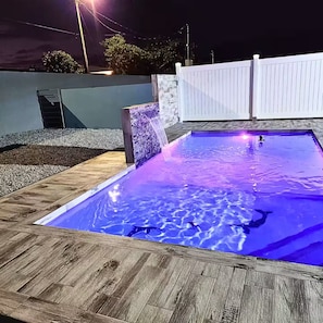 Una piscina rectangular con caída de agua y una terraza de madera alrededor.
