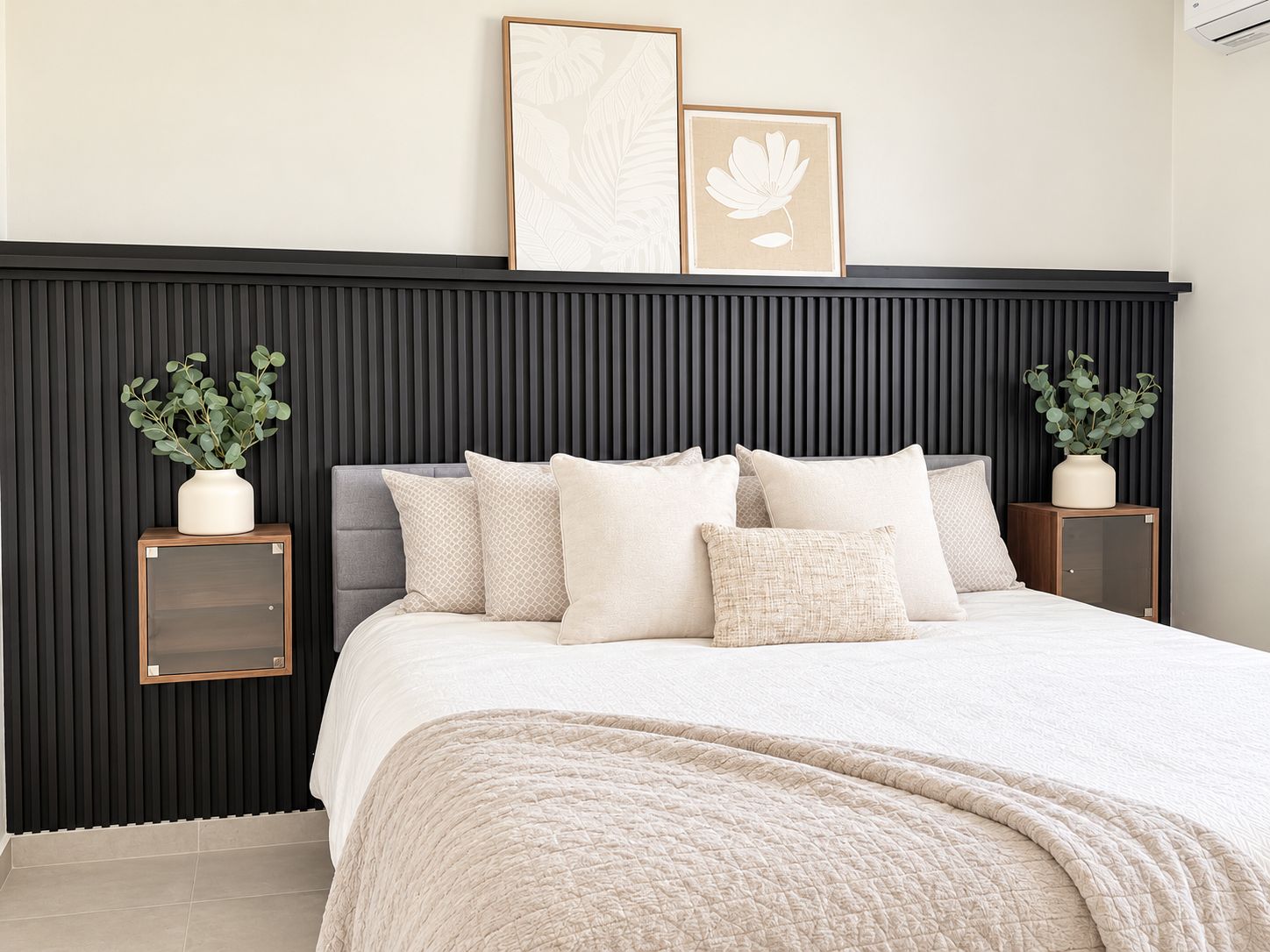 A bedroom with a bed, pillows, a bedside table, a wall-mounted air conditioner, and framed artwork.