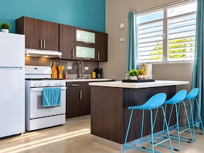 Una cocina moderna con una isla central, taburetes de bar y vistas al exterior.