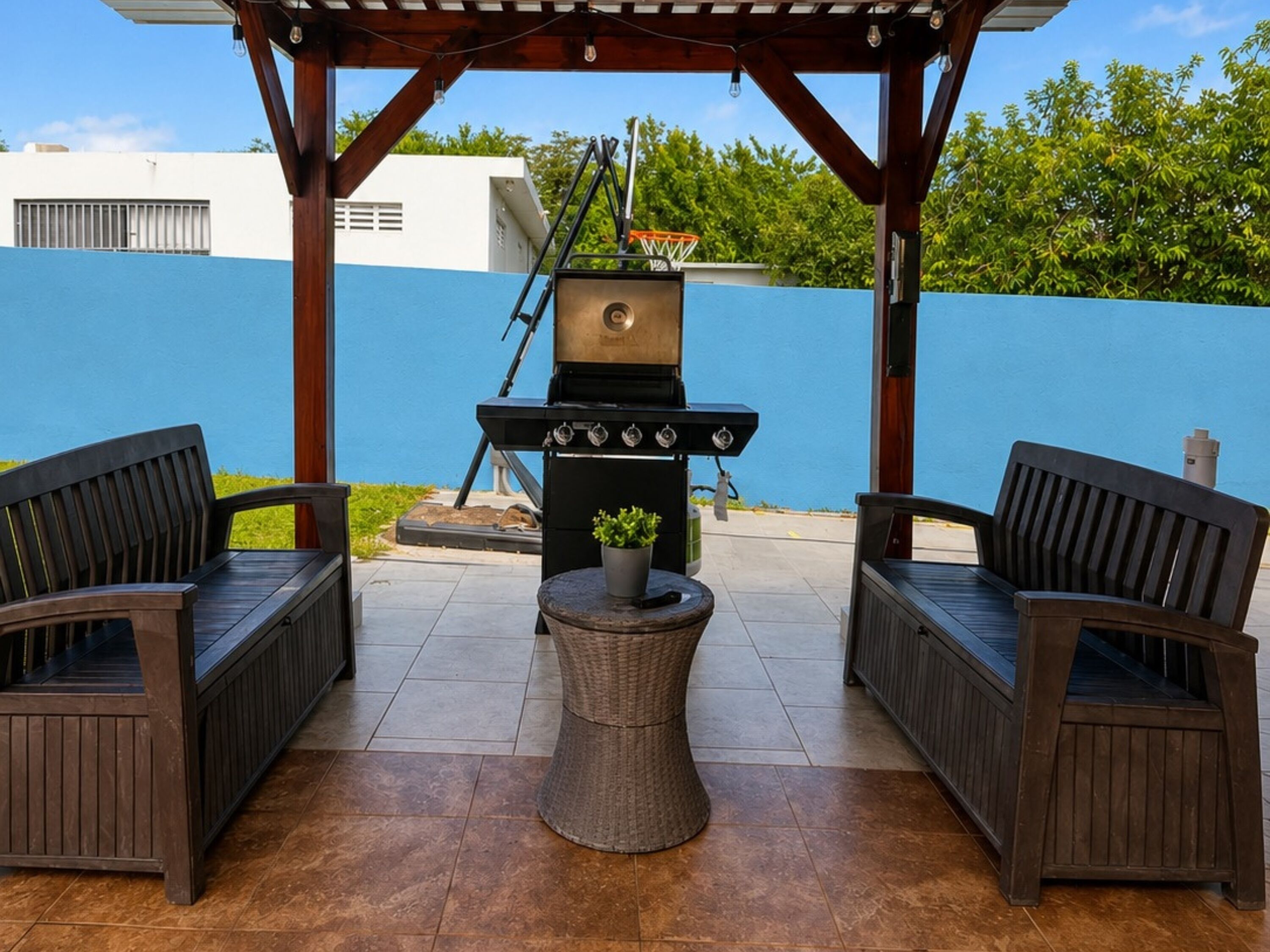 Une terrasse extérieure avec un barbecue, deux fauteuils en osier et une petite table ronde.