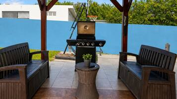 Un patio al aire libre con una parrilla, dos sillas de mimbre y una pequeña mesa redonda.