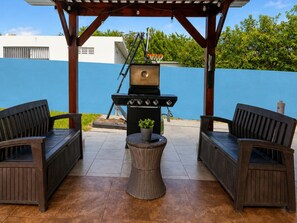Un patio al aire libre con una parrilla, dos sillas de mimbre y una pequeña mesa redonda.