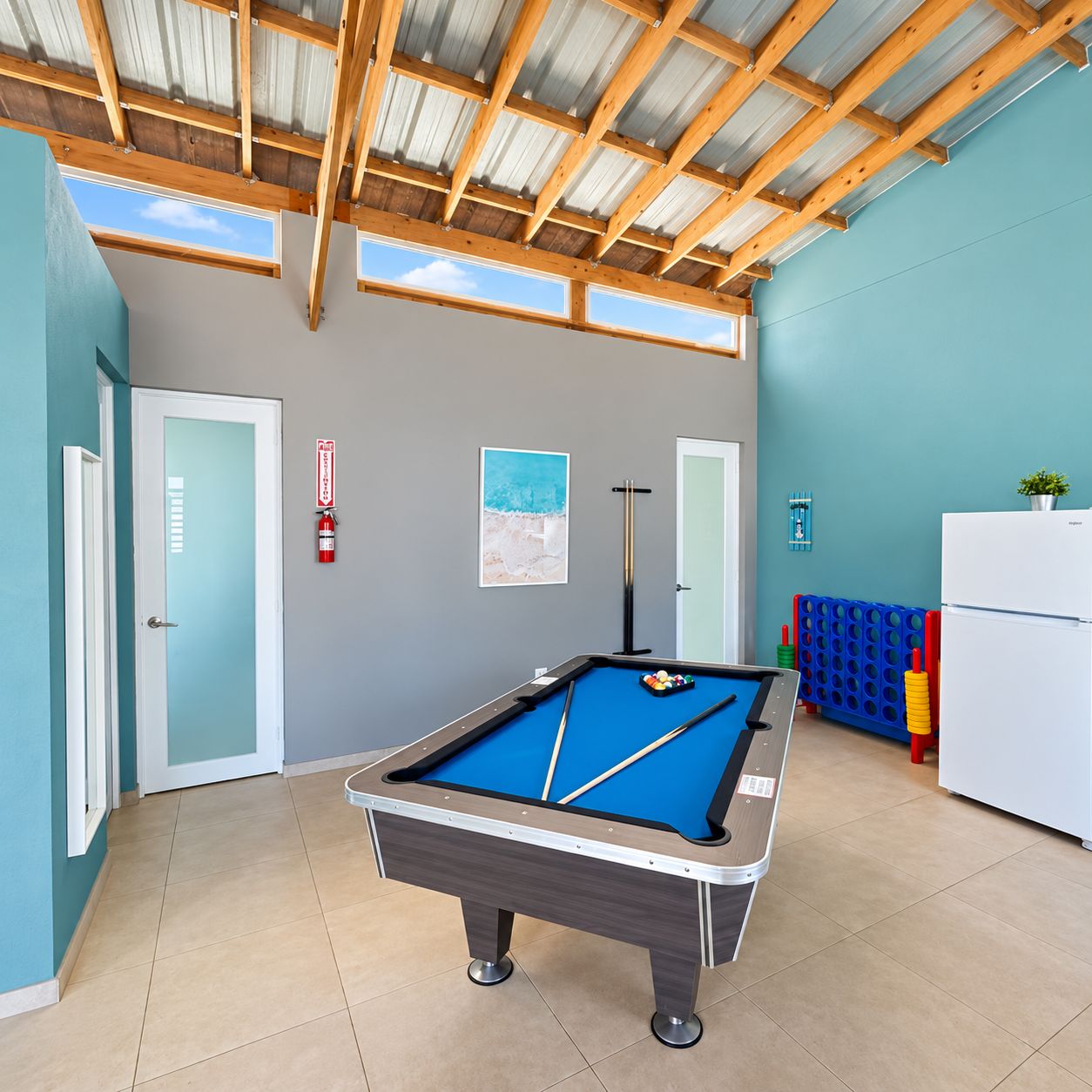 A pool table in a room with teal walls, a wooden ceiling, and a white refrigerator.