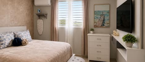 Un dormitorio con cama, televisor, cómoda y un cuadro.