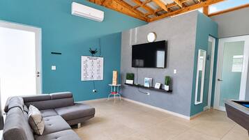 A modern living room with a sectional sofa, a flat-screen TV mounted on the wall, and a pool table.