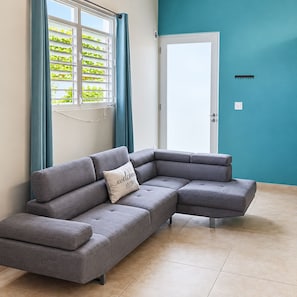 Una sala moderna con un sofá seccional gris, una pared de acento color turquesa y un ventanal con vistas a zonas verdes.