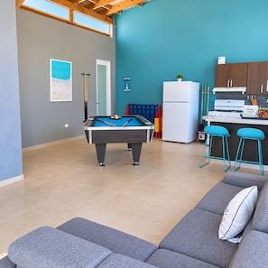 A modern living space with a pool table, a sofa, and a kitchen area.